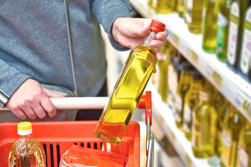 Anonymous person purchasing olive oil in a glass bottle at the grocery store.