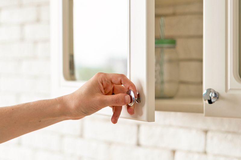 Anonymous pulling a kitchen cabinet open by its round, chrome pull.