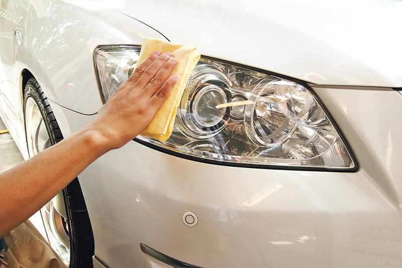 Anonymous person wiping car headlights with a yellow microfiber cloth.