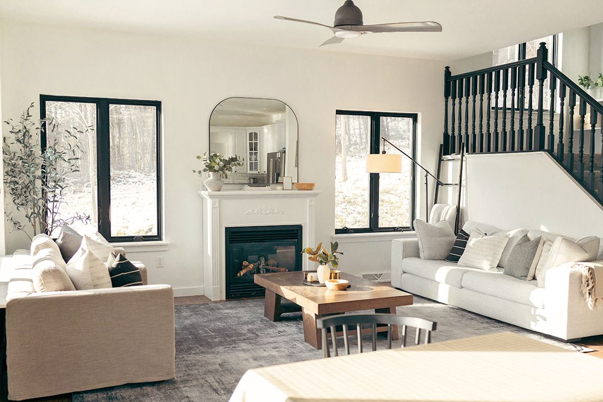 A mostly-white, modern living room with black accents, including black-framed windows, a black fireplace surround, and a black stair railing.