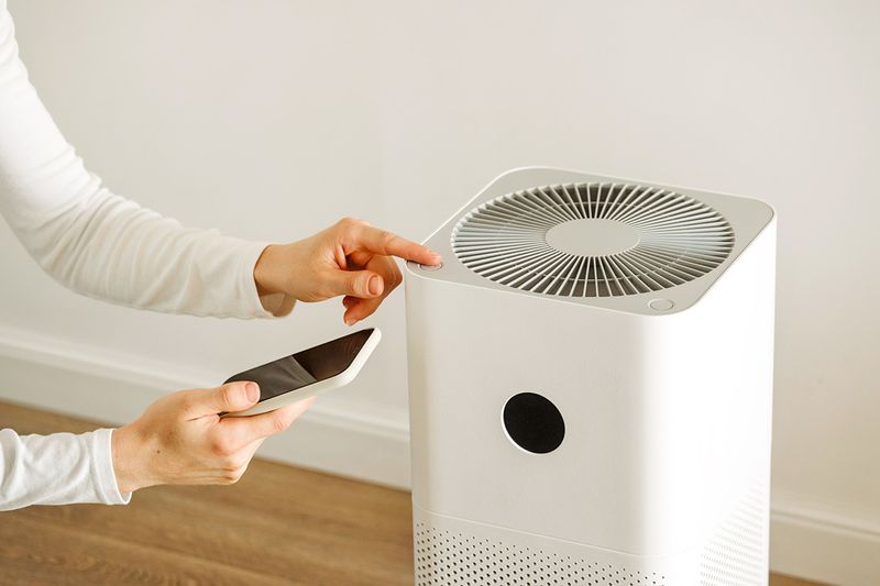 A person pressing the power button on an air purifier while holding their phone in the other hand.
