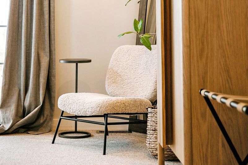 A bouclé accent chair next to a black metal drink table and a woven basket.