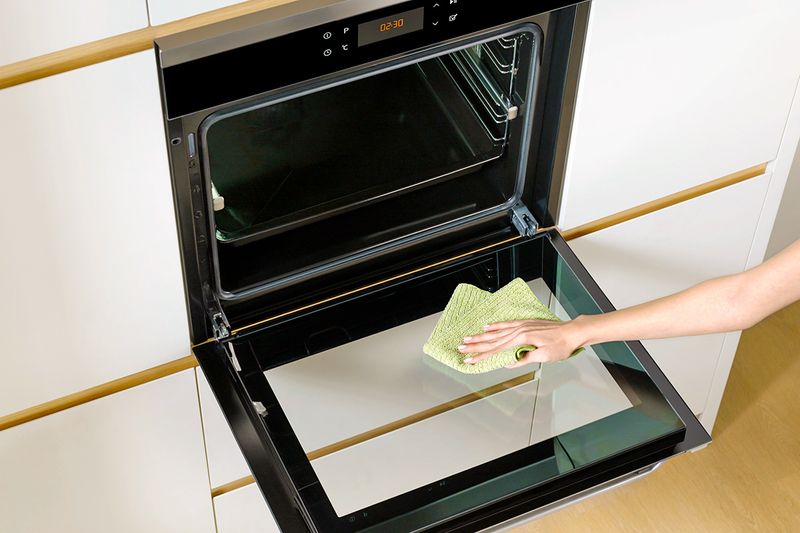 Anonymous person cleaning an open oven with a microfiber cloth.