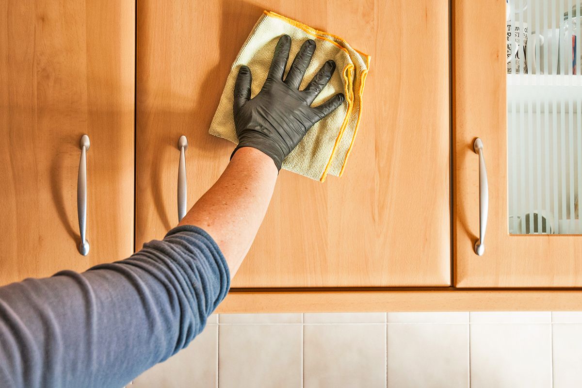 Anonymous person cleaning wood kitchen cabinets with a yellow microfiber cloth.