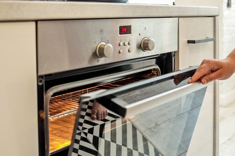 An anonymous person opening an oven door slightly. The oven appears to be on.