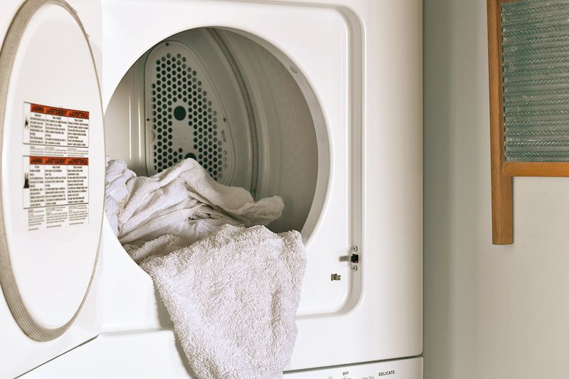 An open dryer with a few white towels cascading out of it.