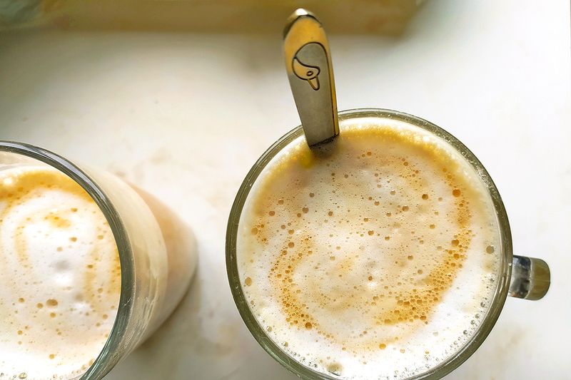 Two coffees in mugs topped with frothed milk.