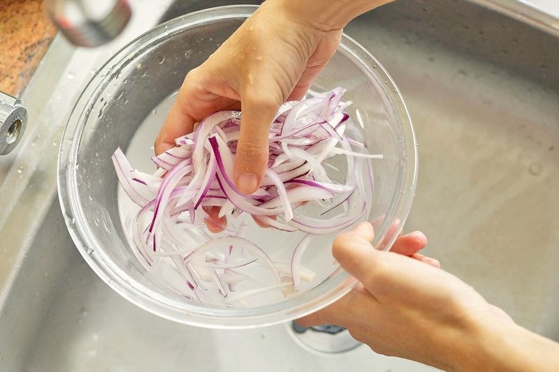 Anonymous person soaking red onion slices in a bowl of water.