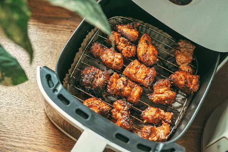 An open air fryer basket showing marinated chicken thighs with nice charring.