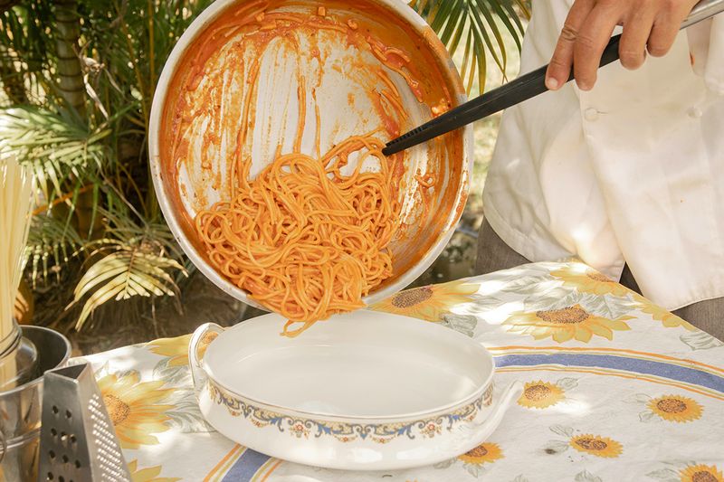 An anonymous person transferring spaghetti in a tomato sauce from a pan to a serving bowl.