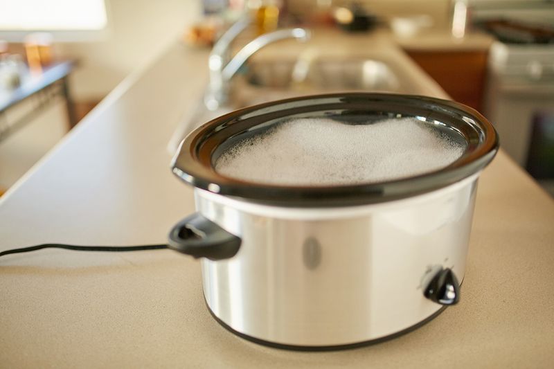 An open slow cooker on a kitchen counter filled with suds.