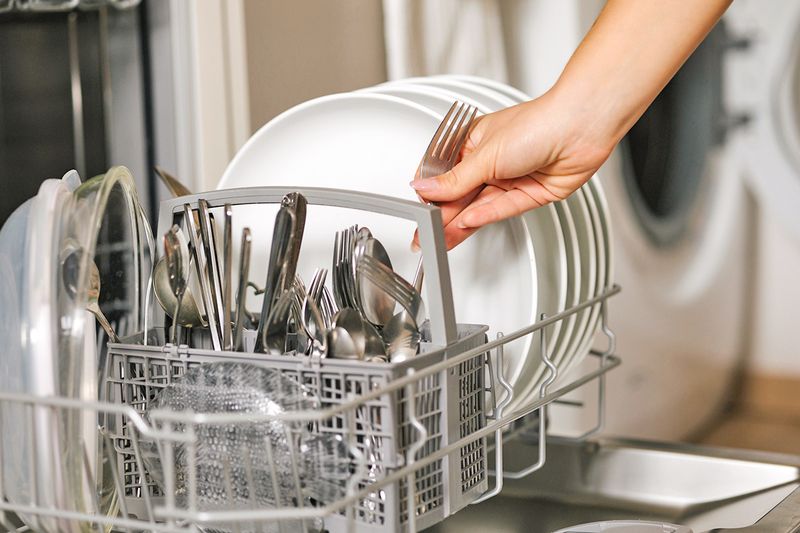 Anonymous person loading silverware into a dishwasher's basket.