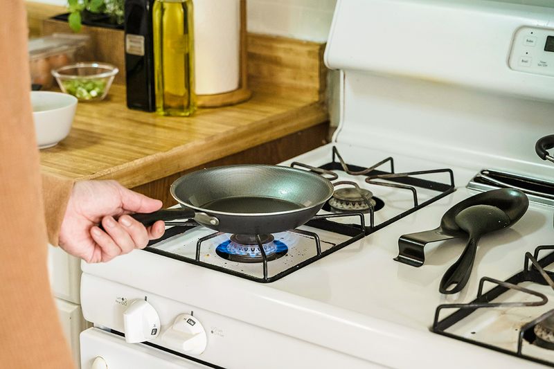 Person holding a nonstick frying pan over a flame on a gas stove burner.