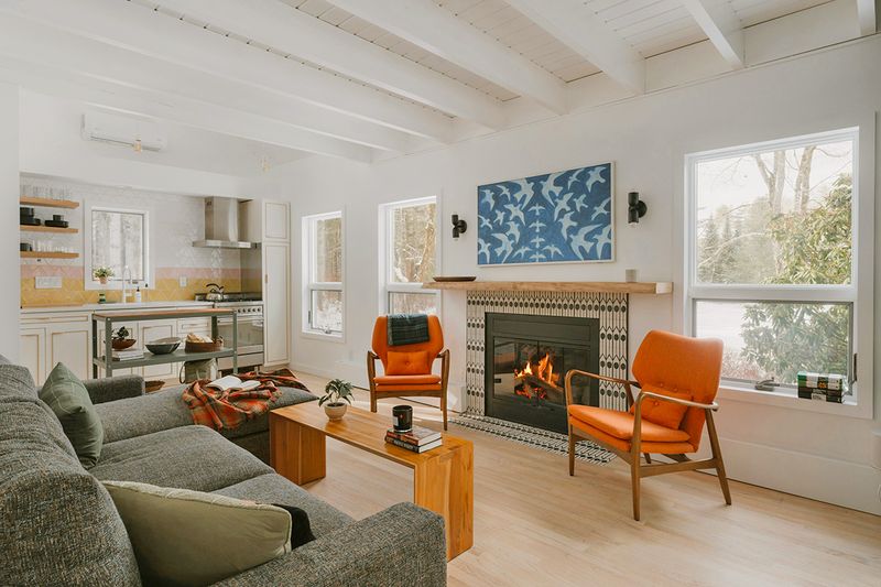 A modern living room with a gray sofa, two orange accent chairs, and a graphic tile fireplace surround.