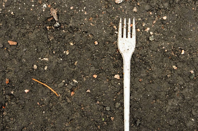 A white plastic fork laying in the dirt.