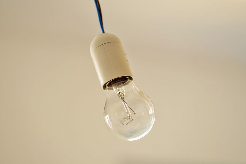 An exposed light bulb hanging from a cord in a white room.
