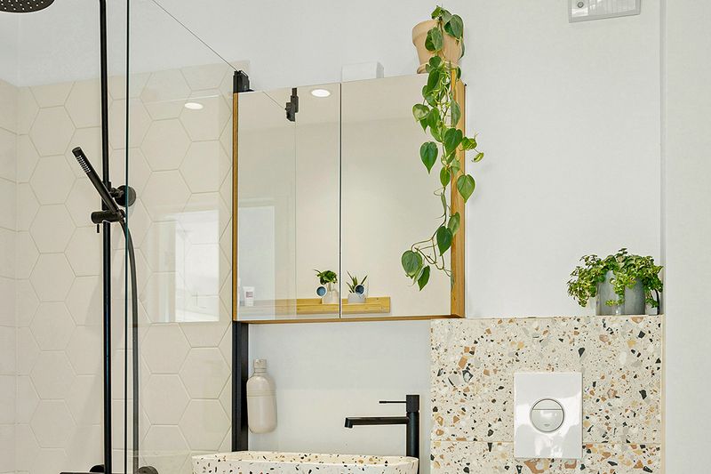 A modern bathroom with a large medicine cabinet, a glass shower, black fixtures, and a terrazzo sink and vanity.