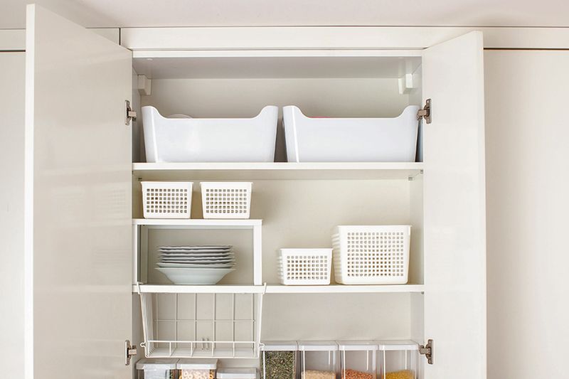An open cabinet door showing two storage bins on the highest shelf and other organizers below.