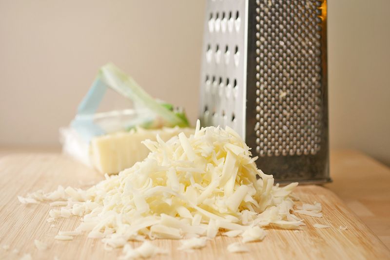 Shredded cheese on a wooden cutting board next to a grater.