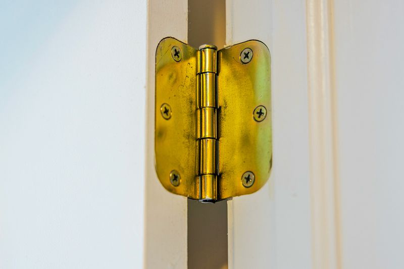A close-up of a brass hinge on a white door.