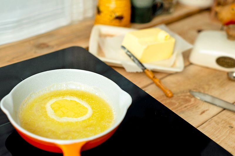 An enameled cast iron pan on a stovetop filled with melted butter.