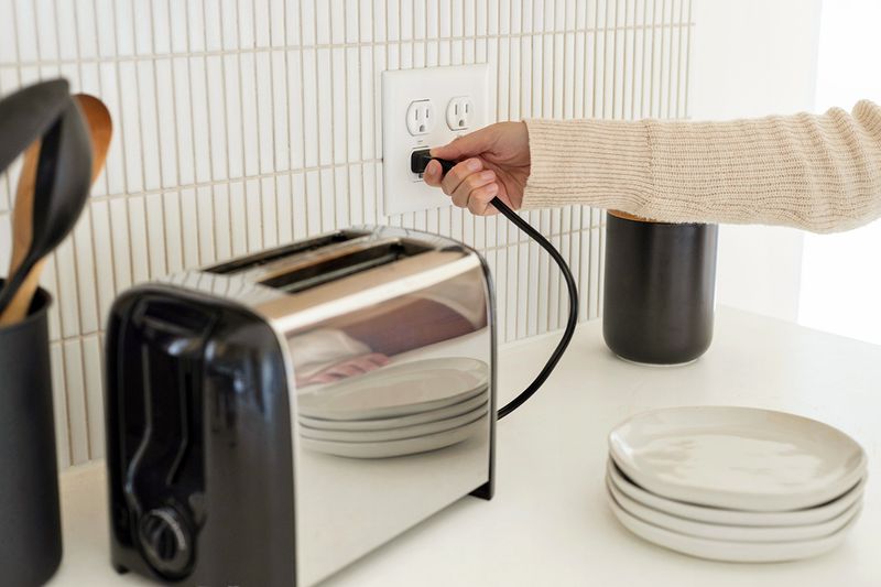 An anonymous person plugging in a metal toaster on a kitchen counter.