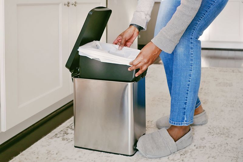 Anonymous woman changing the liner of a kitchen trash can.