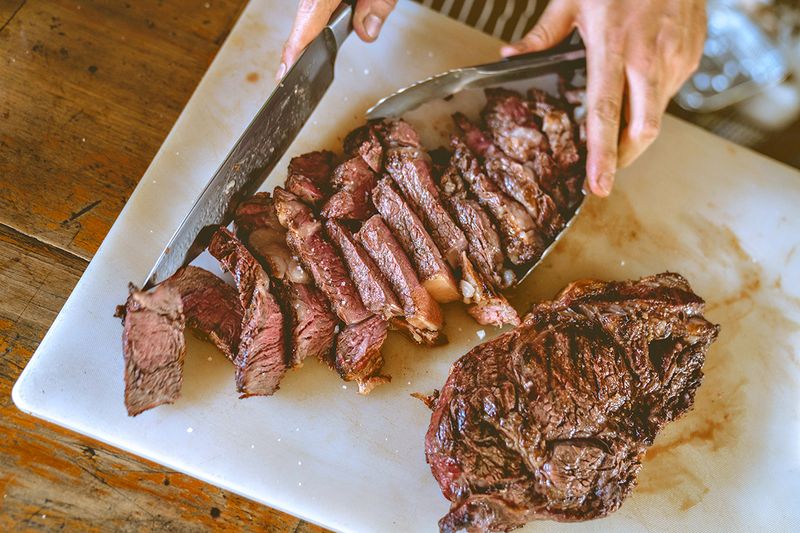Anonymous person cutting a steak into strips on a large white serving platter.
