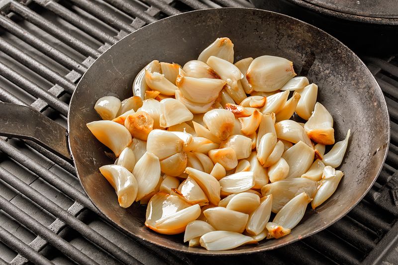 Toasted garlic cloves in a small skillet on grill grates.