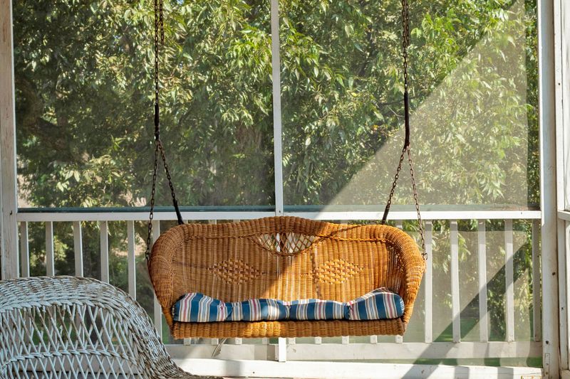 A screened-in porch with a wicker porch swing.