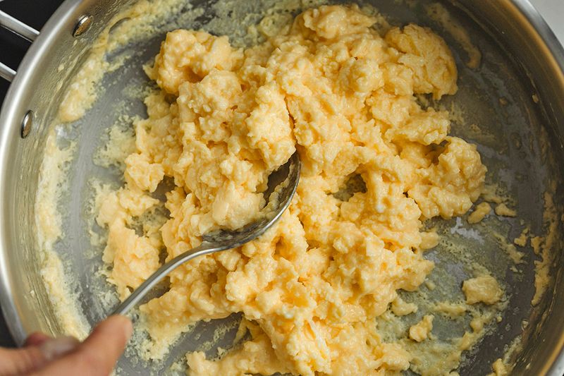Close-up shot of someone serving scrambled eggs from a skillet using a spoon.