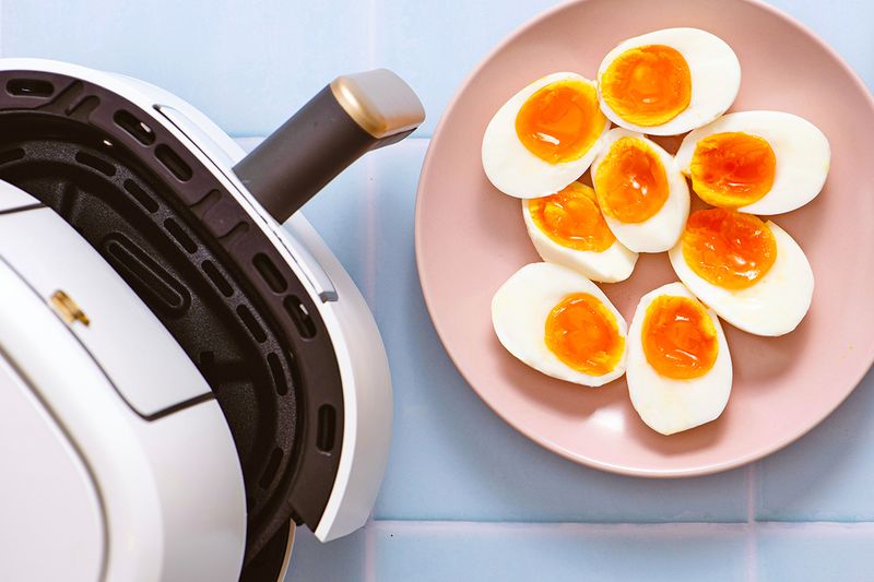 An open air fryer next to a plate of sliced-open, hard-boiled eggs.