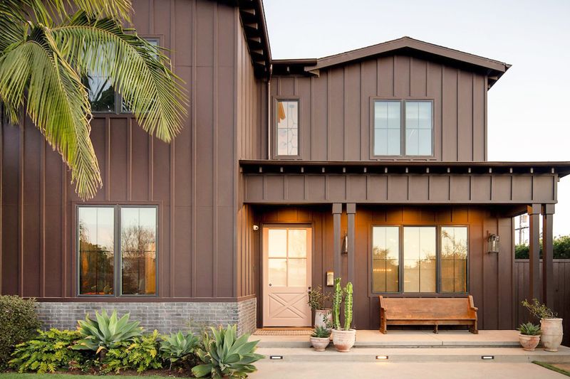 A dark brown, farmhouse-style home with a light pink front door.