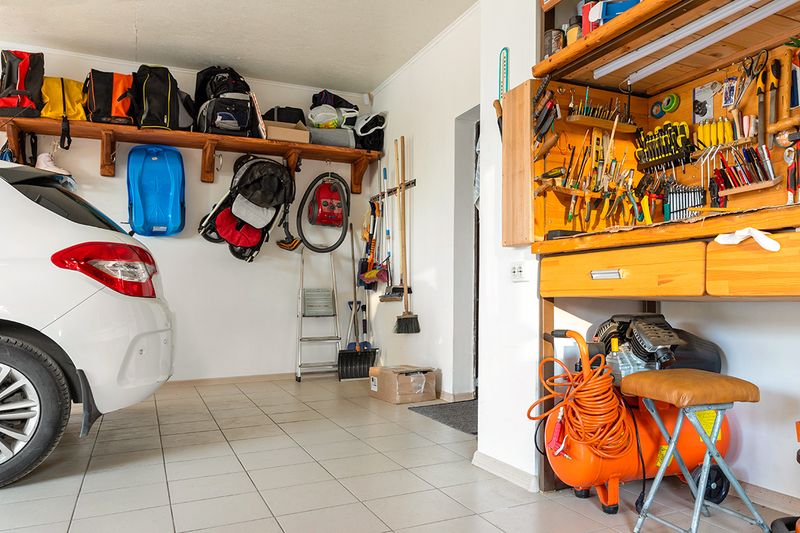 A crowded garage with built-in storage shelves, a workbench, and a parked car.