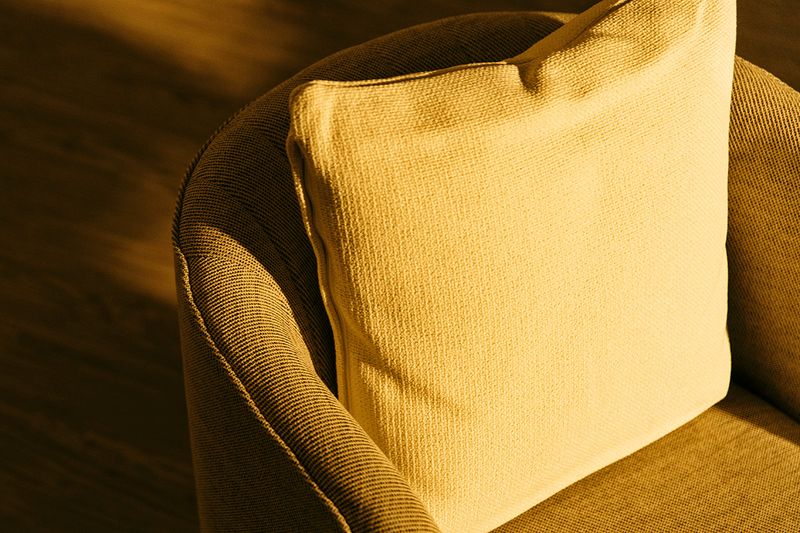 A close-up shot of a barrel chair covered in yellow fabric with the sun shining on it.