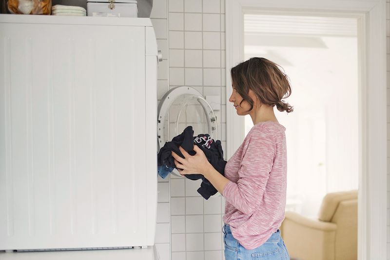 Young woman loading clothes into a front-loading dryer.