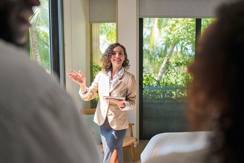 A young, female real estate agent showing a house to two out-of-focus people.