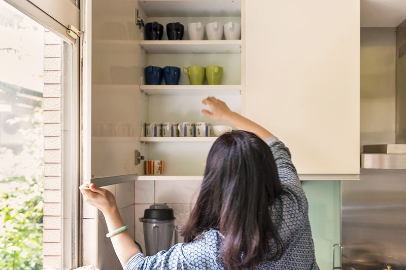 Anonymous woman choosing a coffee mug from an open kitchen cabinet.