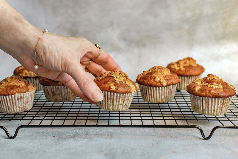 Anonymous person reaching for a muffin on a cooling rack.