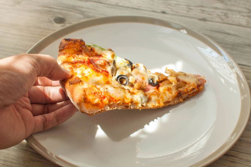 An anonymous person picking up a slice of supreme pizza that's resting on a white ceramic plate.