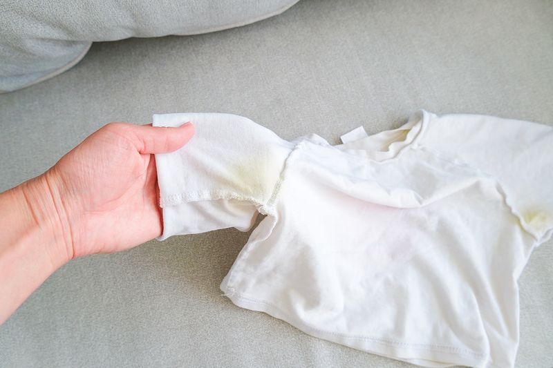 Anonymous person inspecting a white T-shirt with yellow stains under the armpits.