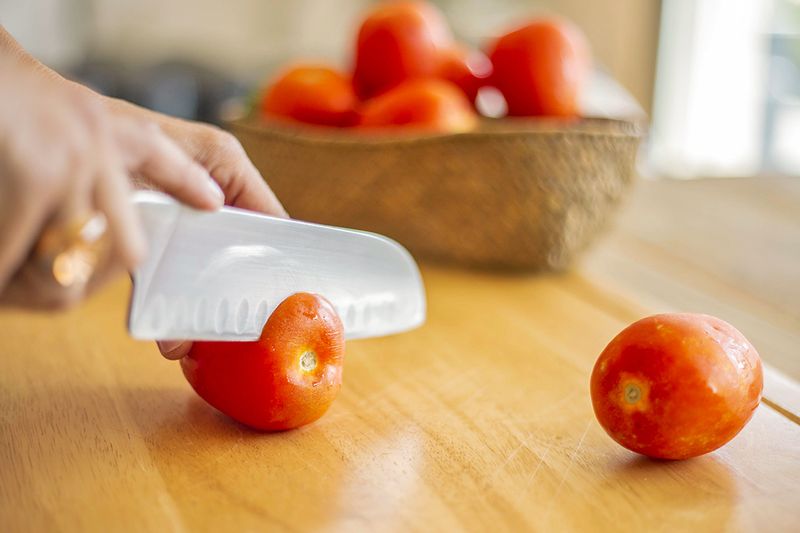 Anonymous person slicing off the calyx of a store-bought tomato with a chef's knife.