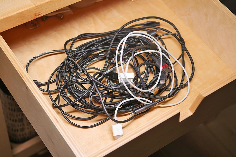 An open drawer revealing a tangled mess of black and white charging cables.