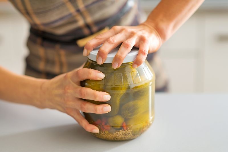 Close-up of anonymous person attempting to open a large, clear glass pickle jar.