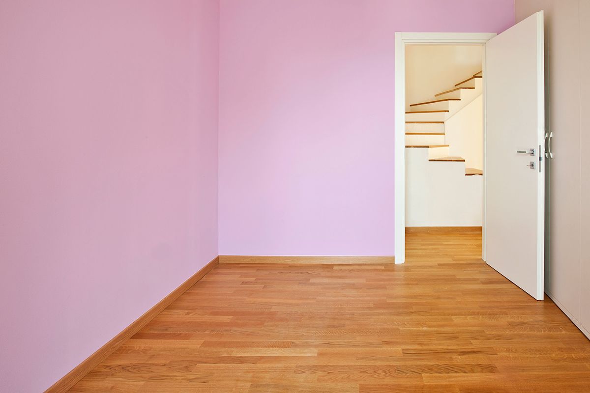 Empty pink room with hardwood floor and white door open up to white staircase.