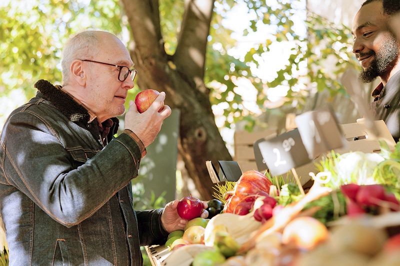 Elderly man smells apples near farmers market stand