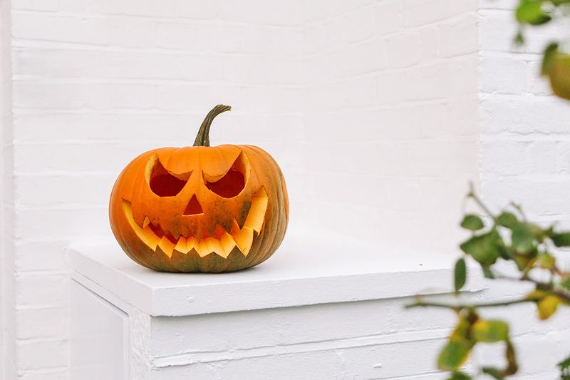 Carved Jack-o-lantern with scary smile against white brick house