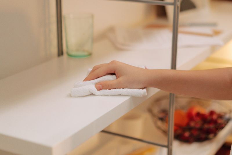 Close-up of a person cleaning a white shelf with a microfiber cloth