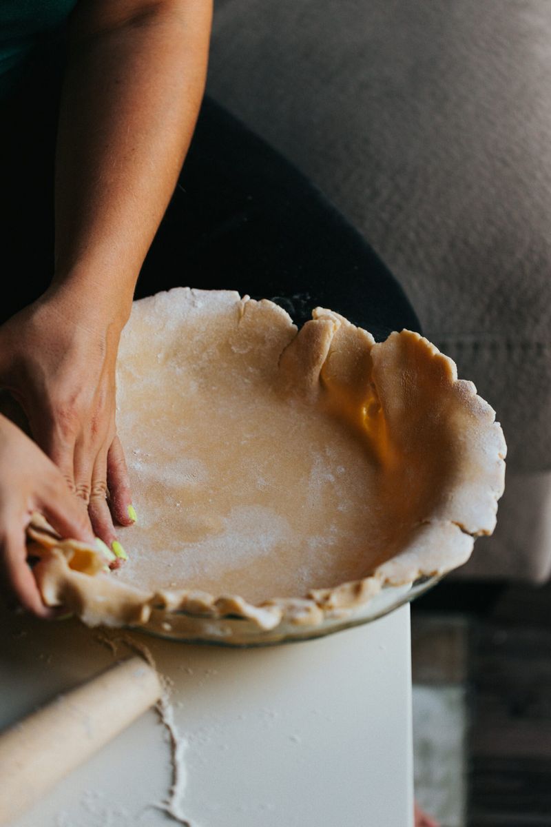 Hands shaping unbaked pie crust in tin